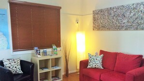 A living room with a red sofa, a black armchair, a wooden coffee table, and a bookshelf. - Biloela Countryman Motel (Biloela)