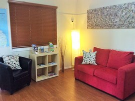 Una sala de estar con un sofá rojo, un sillón negro, una mesa de centro de madera y una estantería.