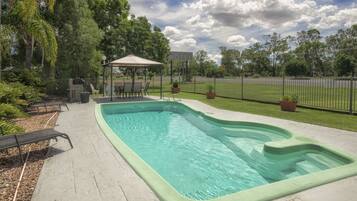 Relax by the serene pool surrounded by a well-maintained lawn and a covered seating area.