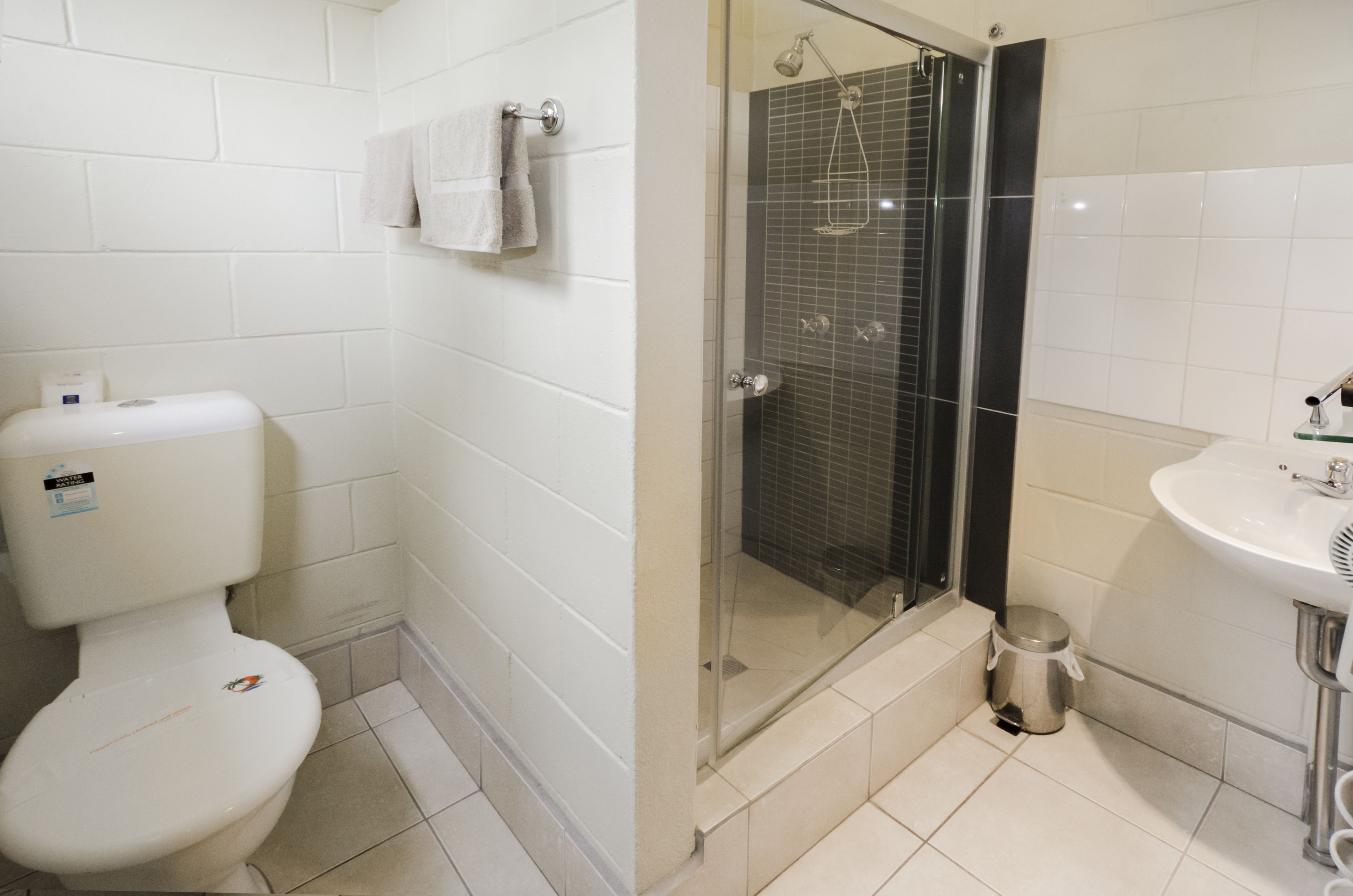 Un baño con inodoro, ducha con mampara de vidrio y lavamanos.
