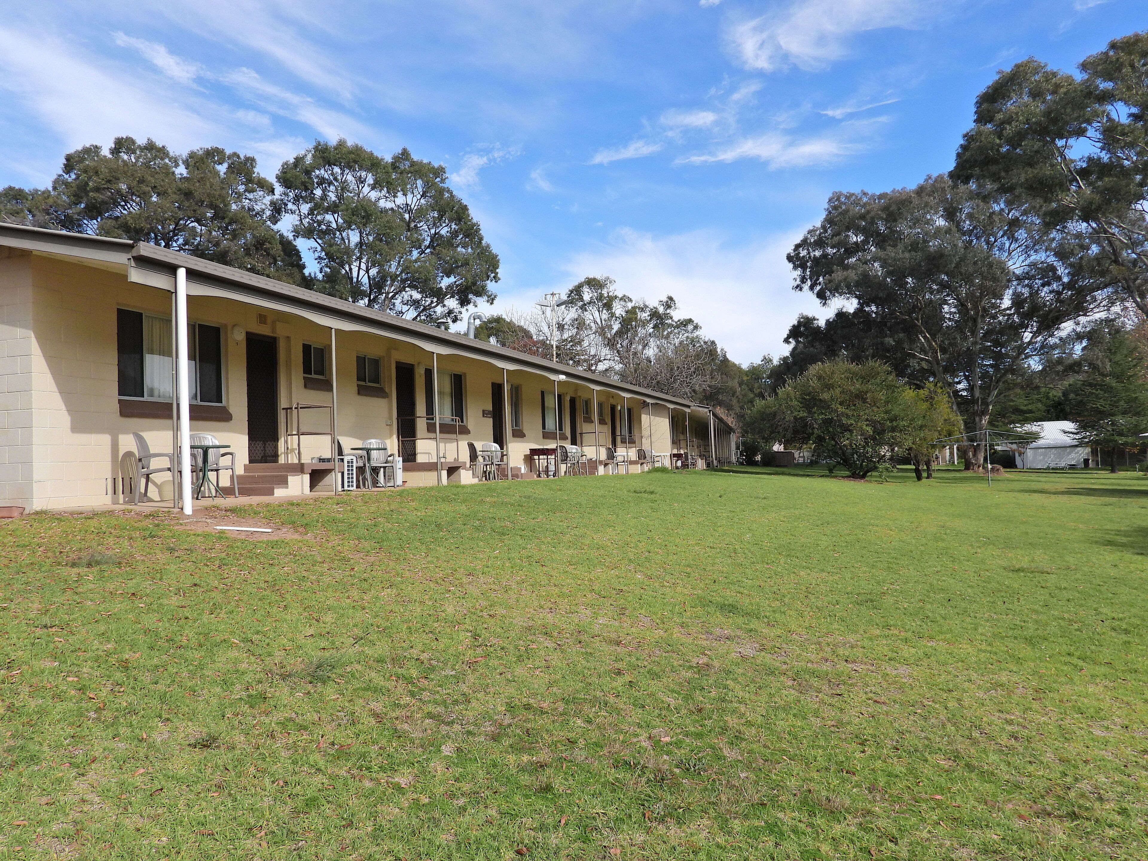 A motel with a covered outdoor seating area and a grassy lawn.