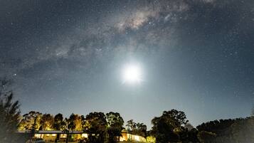 Cielo estrellado con una luna brillante y un edificio con zona exterior techada.