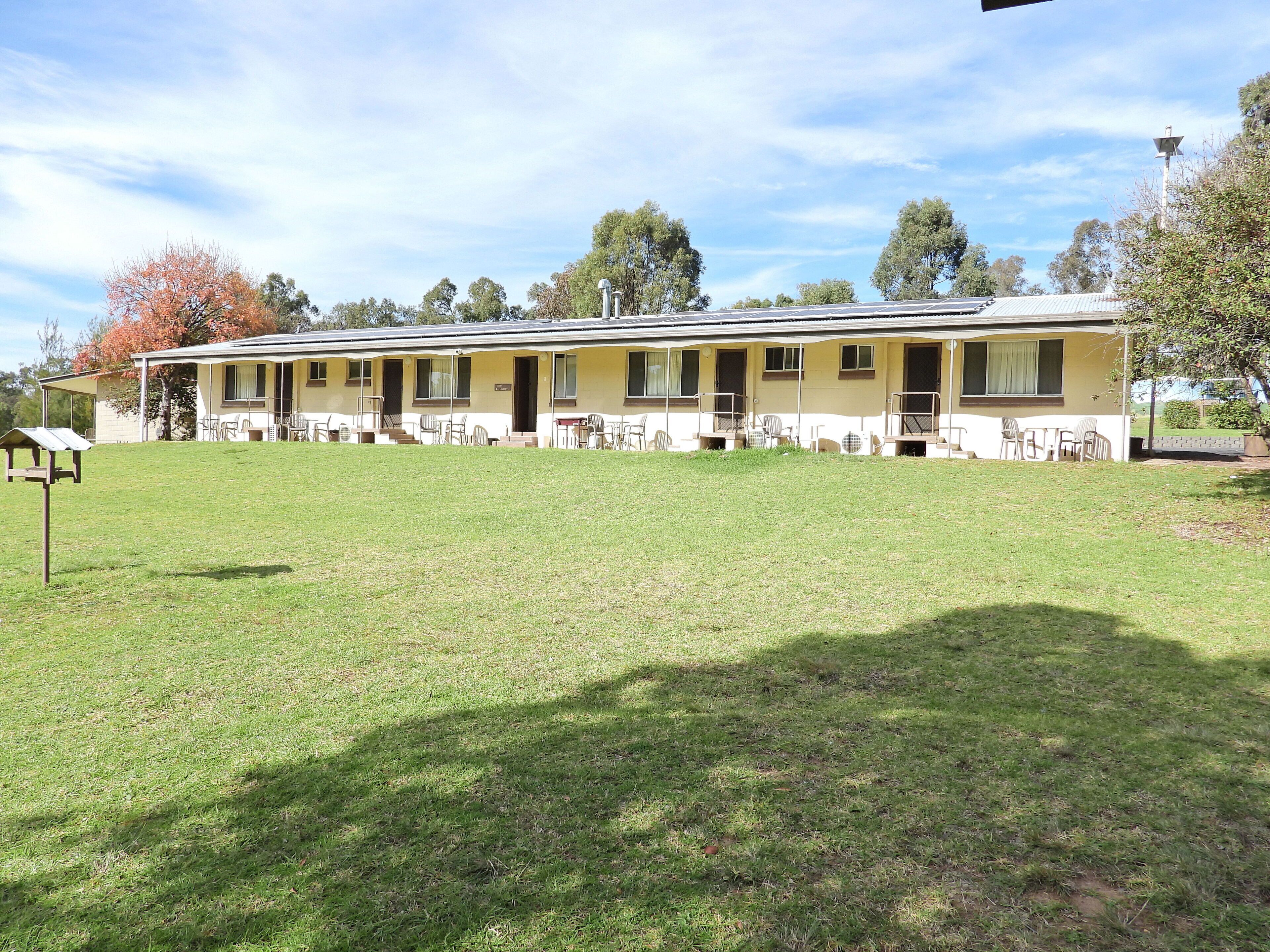 A motel with a covered outdoor seating area and a grassy lawn.
