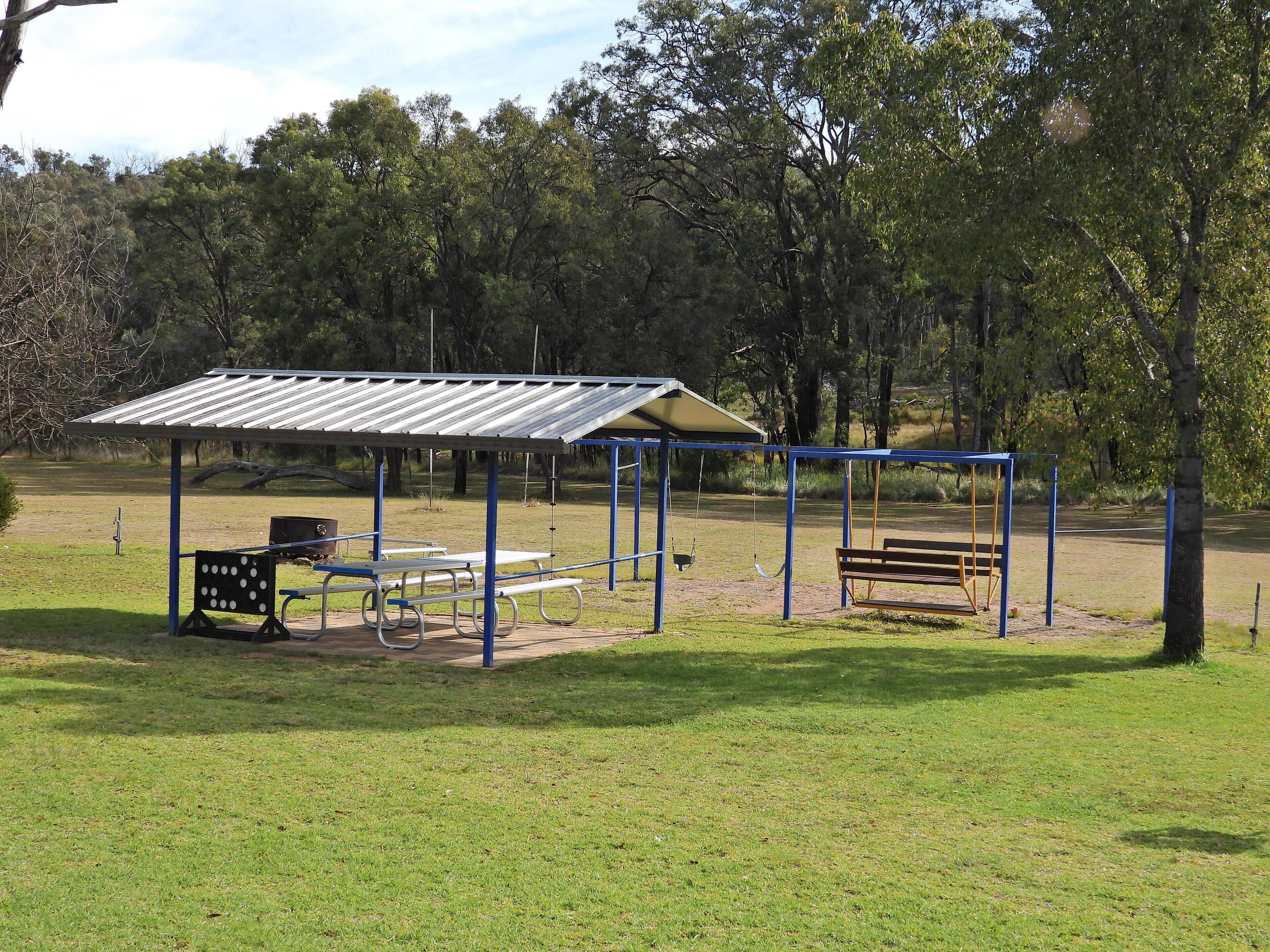 A park with a covered picnic area, benches, and a swing set.