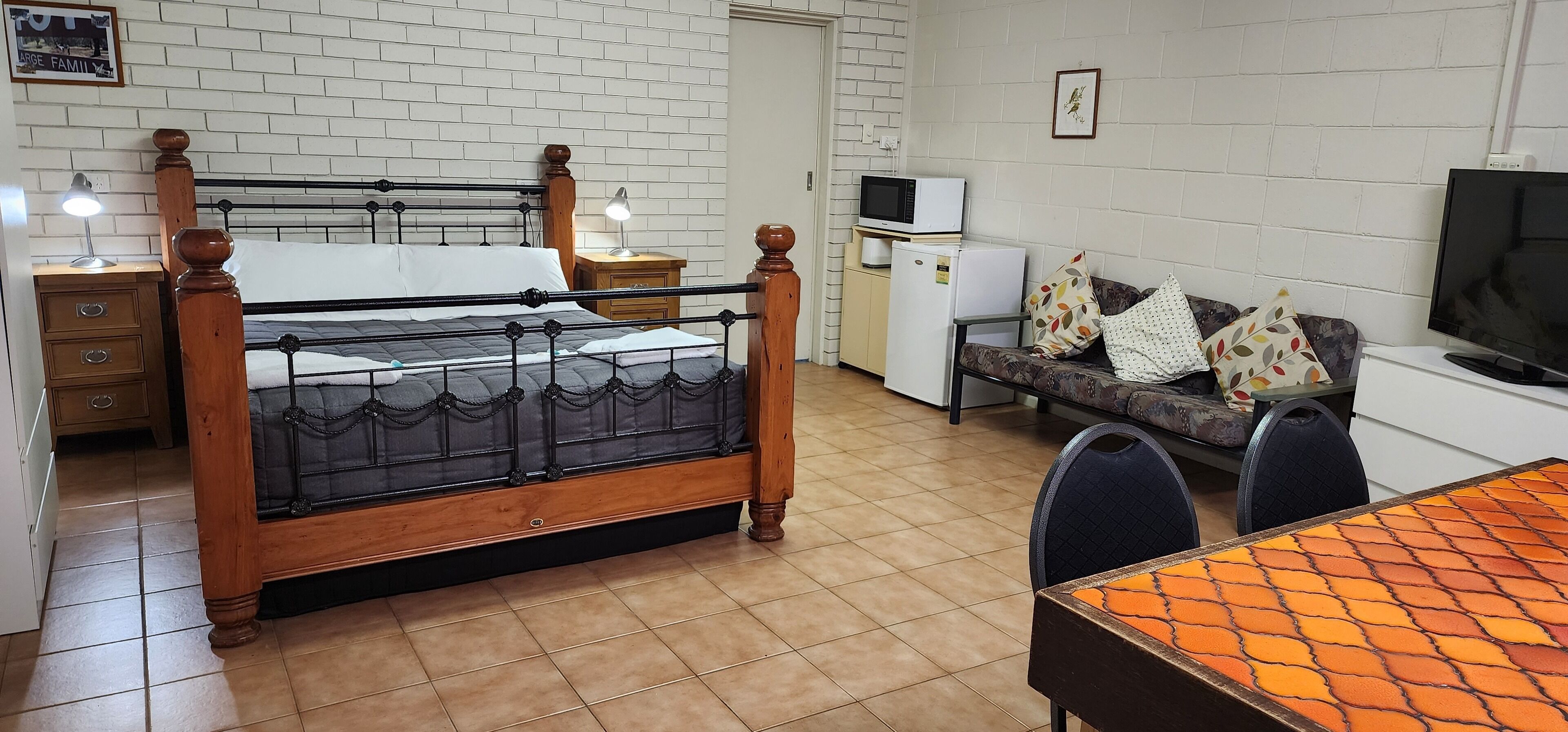 Una camera da letto con un letto in legno, comodini, una scrivania, una sedia, un televisore e un frigorifero.
