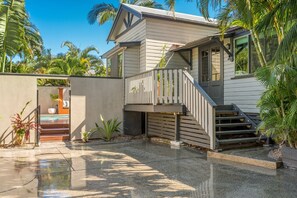 Una casa moderna con una escalera de madera que da a una terraza, rodeada de palmeras.