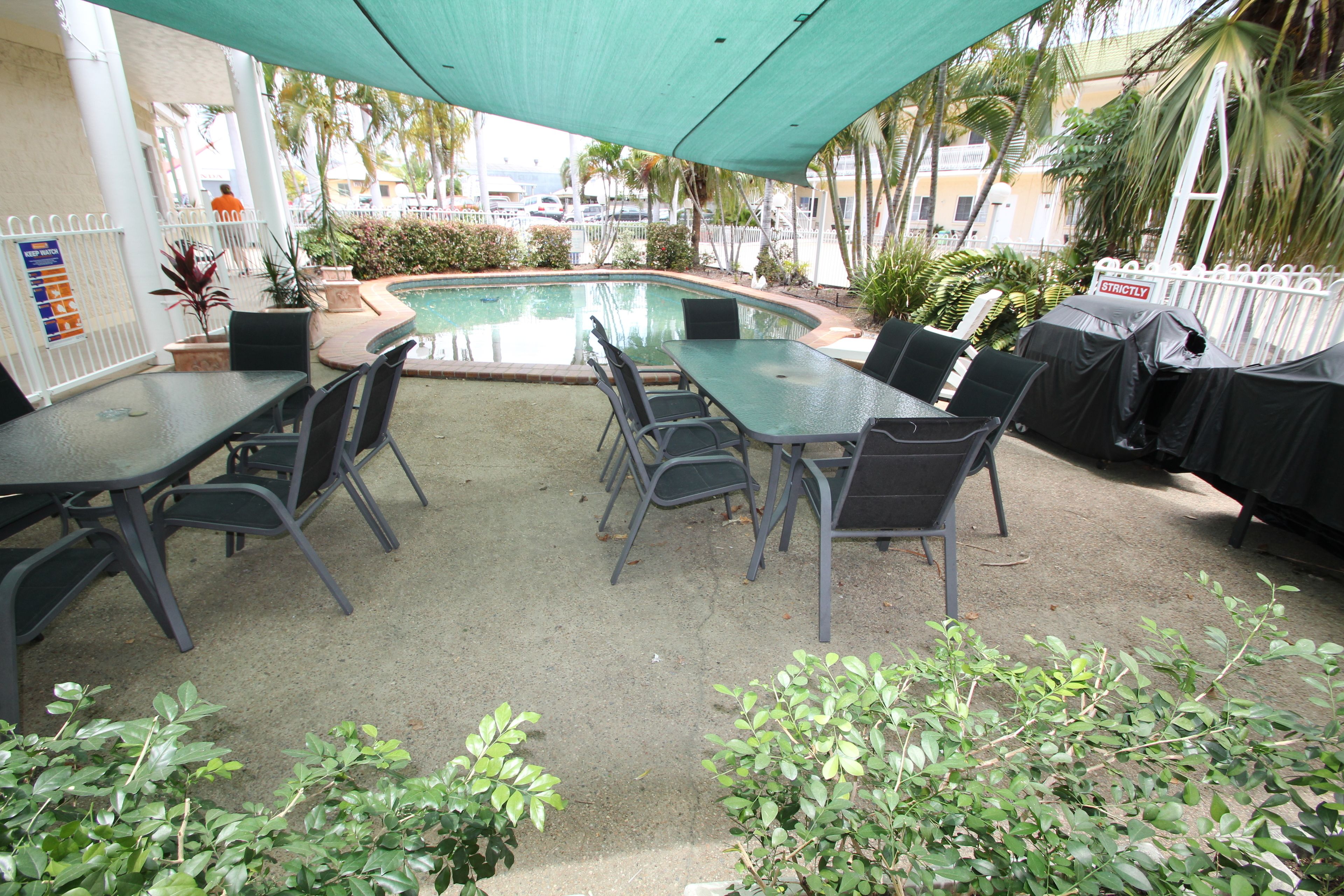 Ein Poolbereich im Freien mit überdachter Lounge-Bereich und Grillplatz.