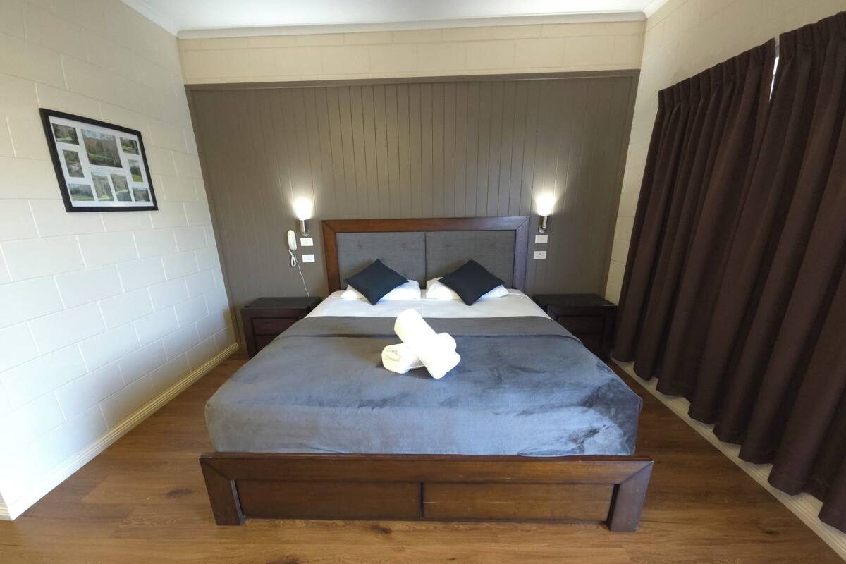 Ein ordentlich bezogenes Bett mit einem dunklen Kopfteil, zwei Nachttischlampen und einem gerahmten Bild an der Wand.
