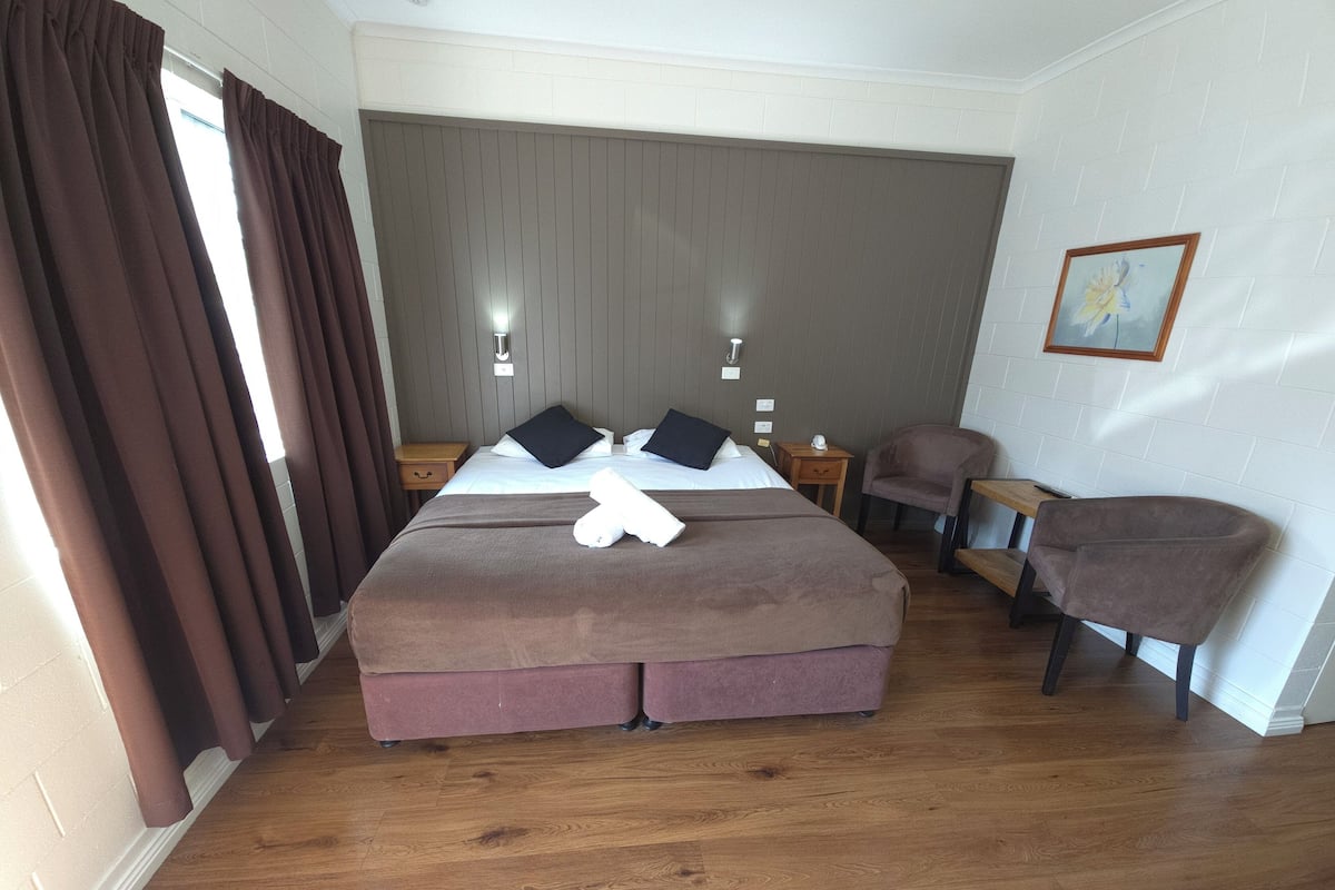Ein Hotelzimmer mit einem großen Bett, einem Sessel, einem kleinen Tisch und einem Nachttisch.