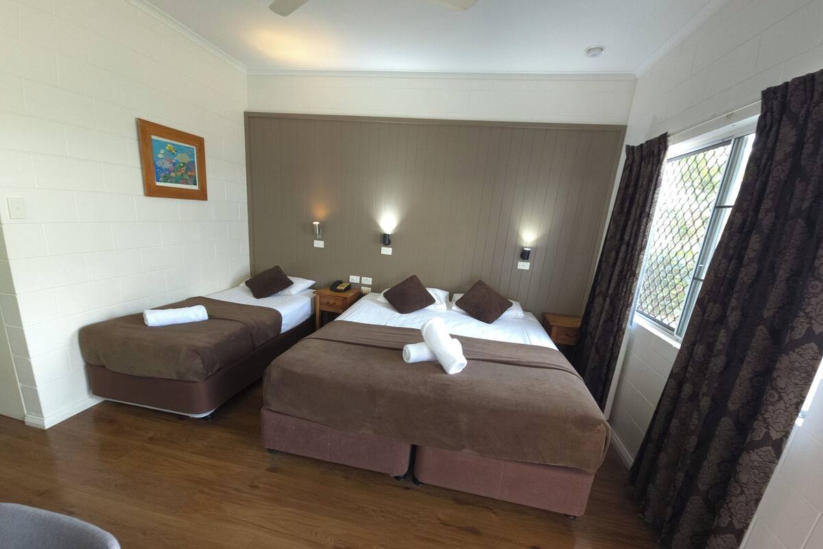 Ein Hotelzimmer mit zwei Betten, Holzboden, Deckenventilator und einem Fenster mit Vorhängen.