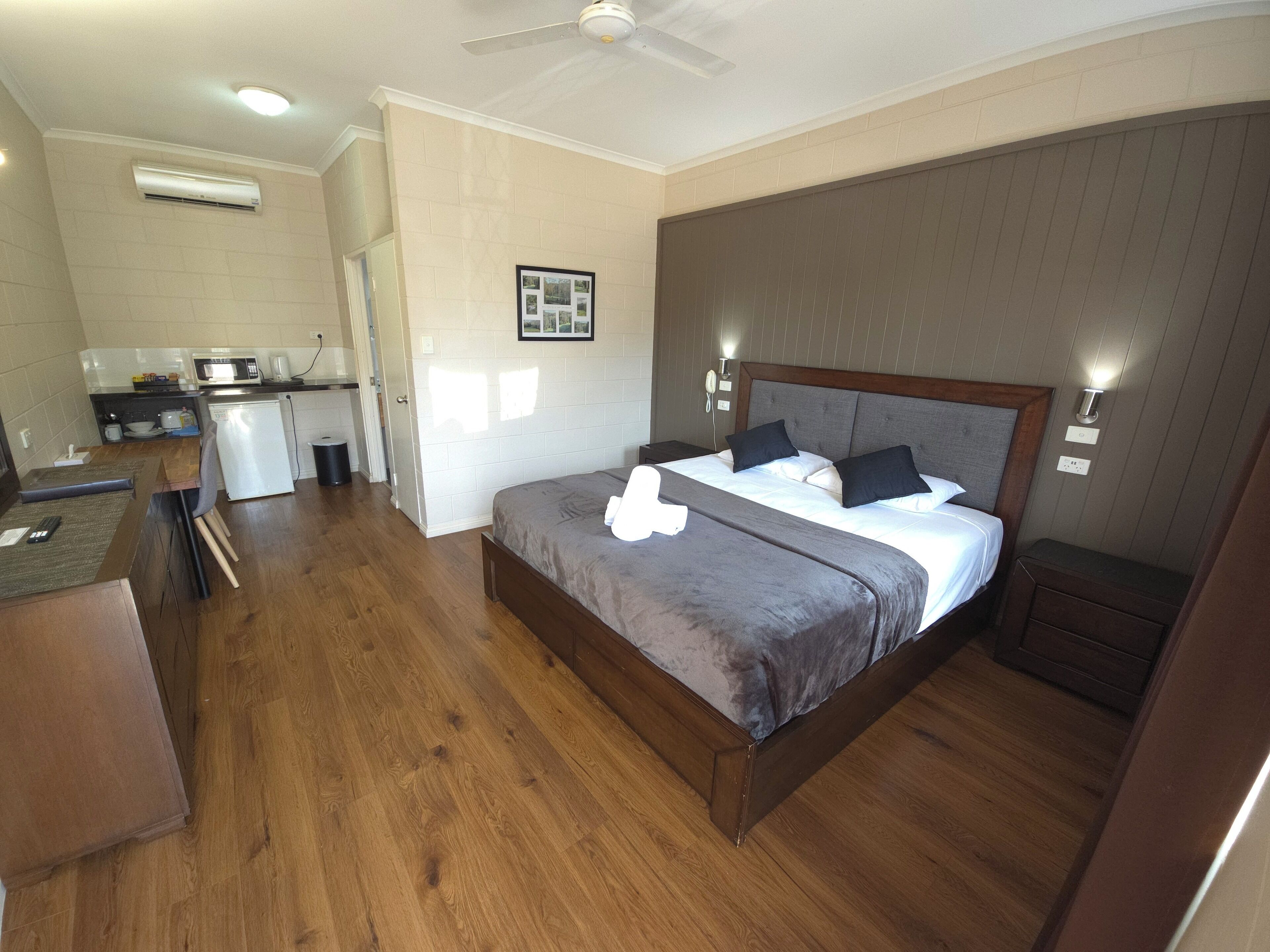 Habitación de hotel con una cama grande, piso de madera, kitchenette y ventilador de techo.