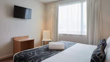 A hotel room with a bed, a TV mounted on the wall, a chair, and a window with curtains.
