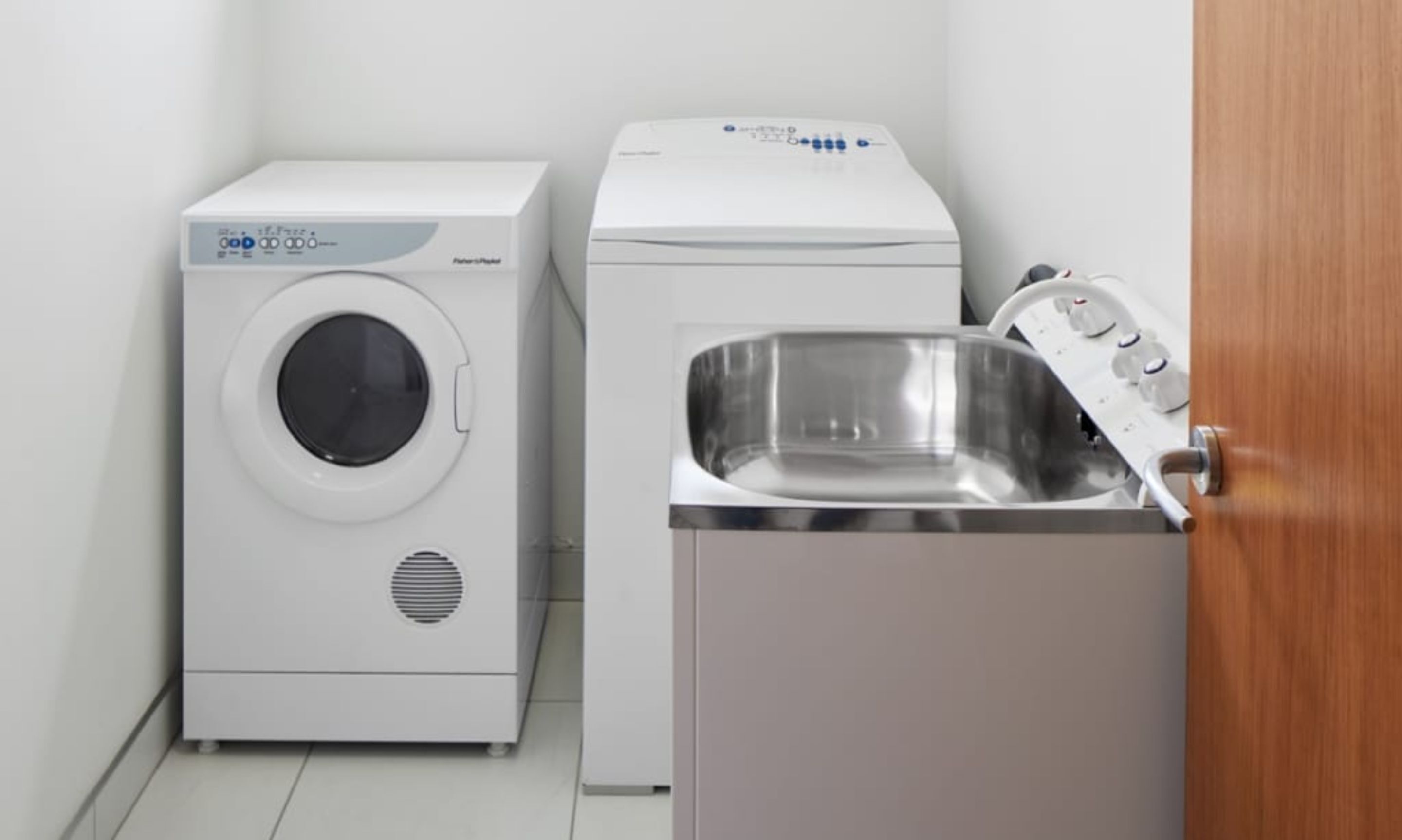 Uma lavanderia com máquina de lavar de carregamento frontal, secadora e pia.