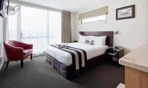 A hotel room with a large bed, a red armchair, a nightstand, and a window with curtains. - Focus Motel And Executive Suites (Christchurch)