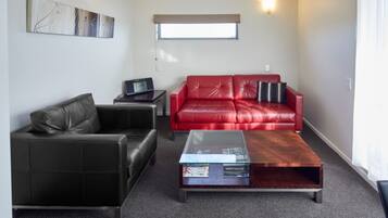 A living room with a black leather sofa, a red leather sofa, a glass coffee table, and a small side table with a laptop.
