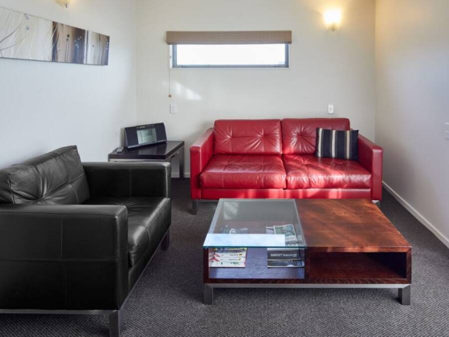 A living room with a black leather sofa, a red leather sofa, a glass coffee table, and a small side table with a laptop.