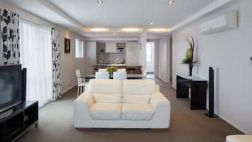 Un salon moderne avec un canapé blanc, un téléviseur à écran plat et un coin repas comprenant une table et des chaises en verre.