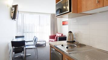 A compact kitchen with a microwave, stove, and a small sink. There is a dining area with a table and chairs, and a red sofa.