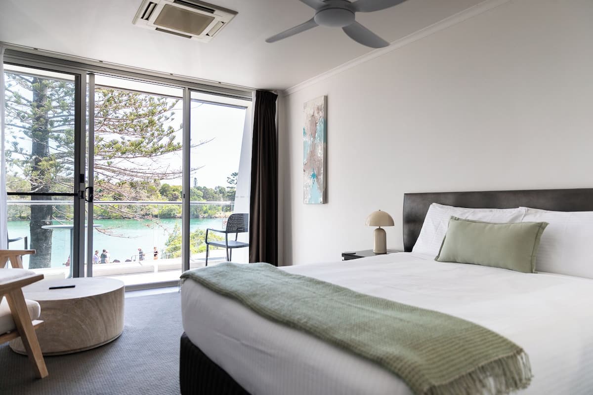 Ein modernes Hotelzimmer mit einem großen Bett, Blick auf einen Pool und einem Deckenventilator.