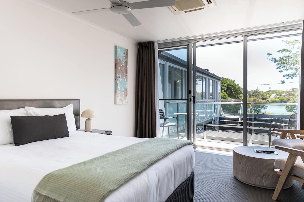 Ein modernes Hotelzimmer mit einem großen Bett, einem Schreibtisch, einem Stuhl und einem Balkon mit Blick ins Freie.