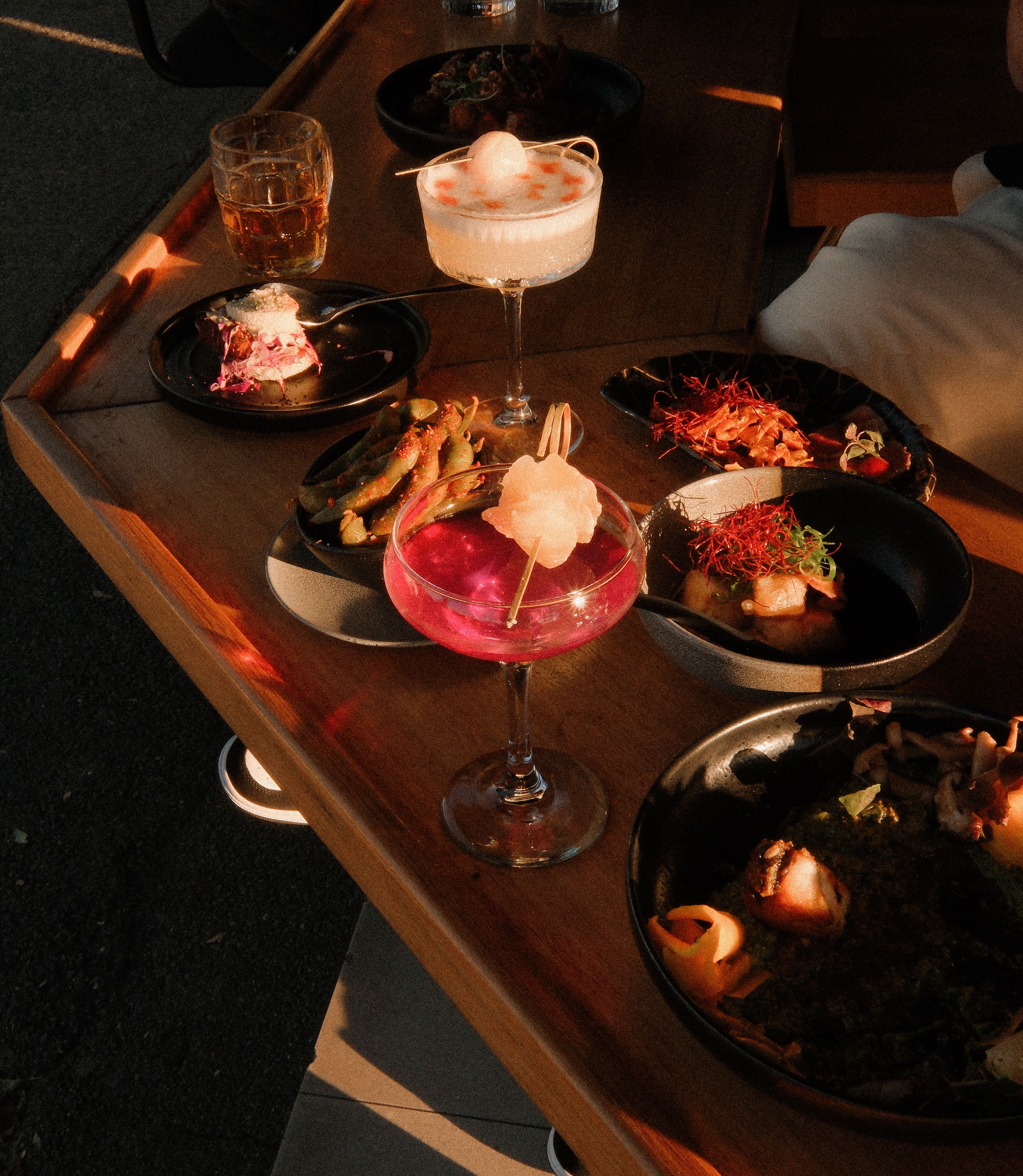 A dining table with various dishes and drinks, including a pink cocktail and a dessert with a scoop of ice cream.