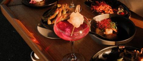 A dining table with various dishes and drinks, including a pink cocktail and a dessert with a scoop of ice cream.