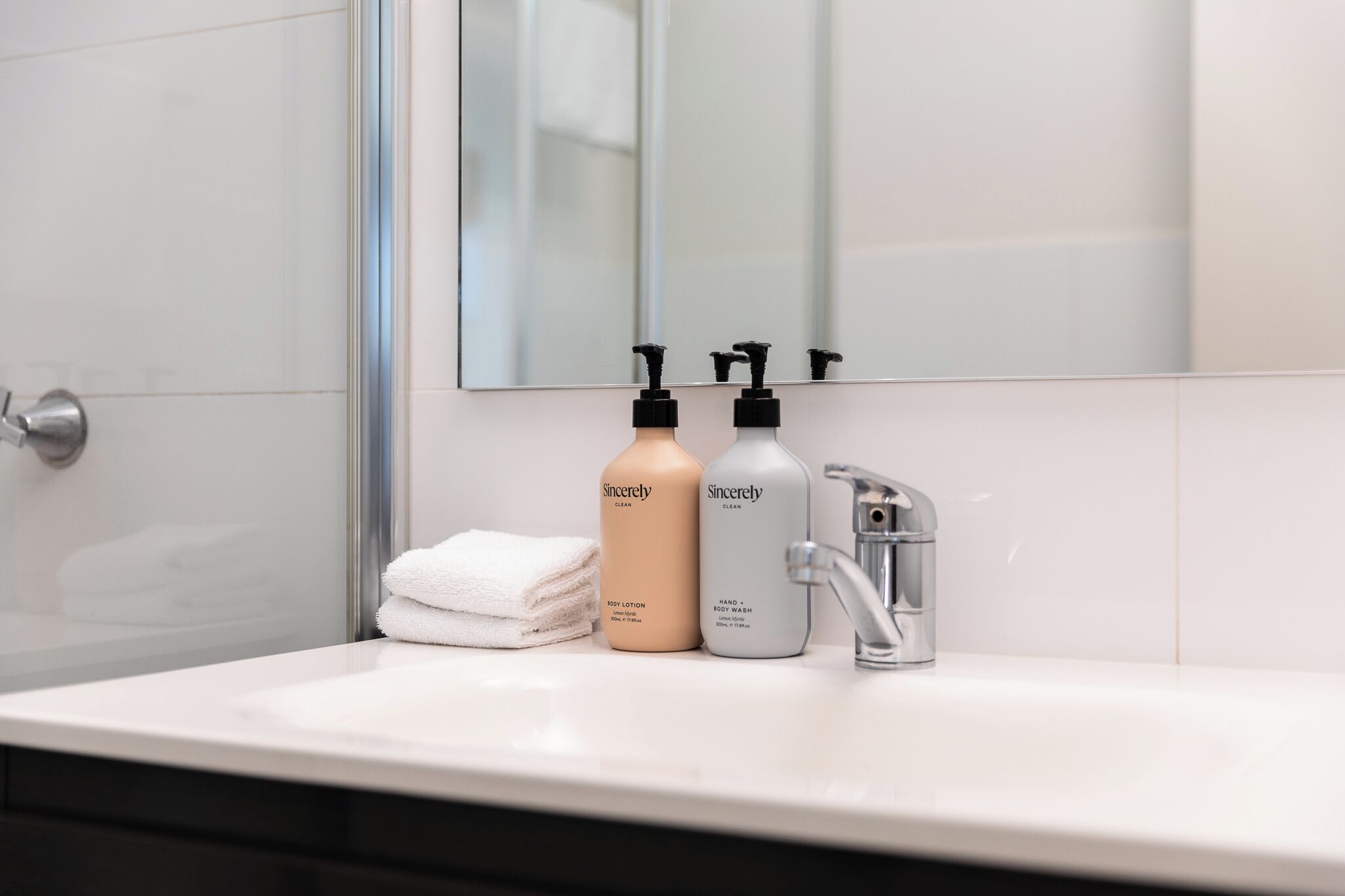 A bathroom with a white sink, two bottles of Sincerely body wash, a towel, and a mirror.