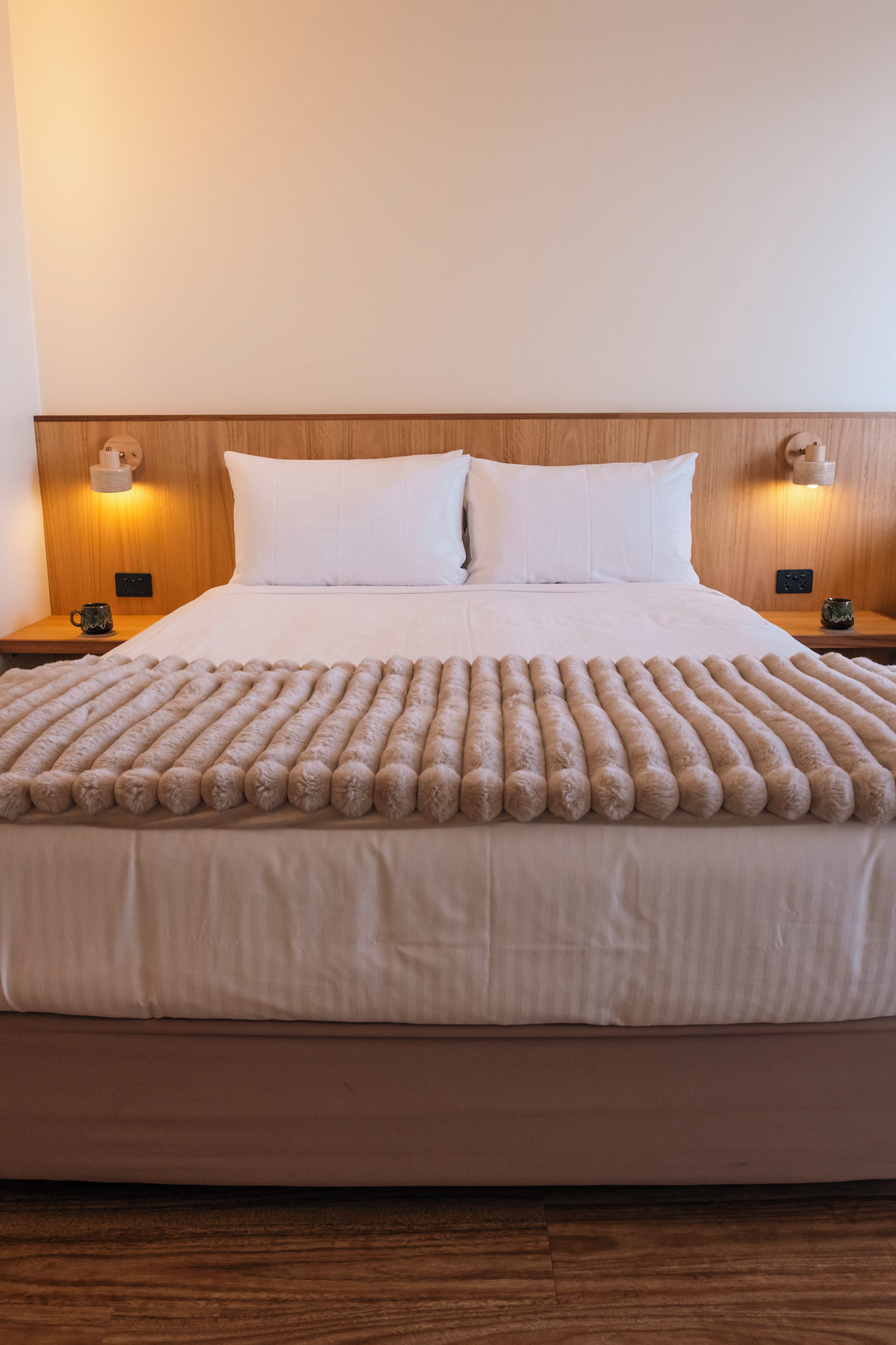 A bed with a fluffy blanket, two bedside tables with lamps, and a wooden headboard.