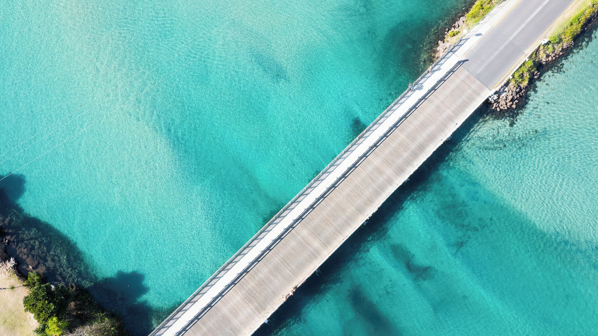 An aerial view of a bridge over clear turquoise water with a road running parallel to it.