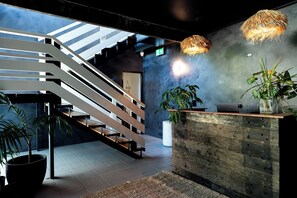 Un área de recepción moderna con un mostrador de madera, una escalera y plantas en macetas.