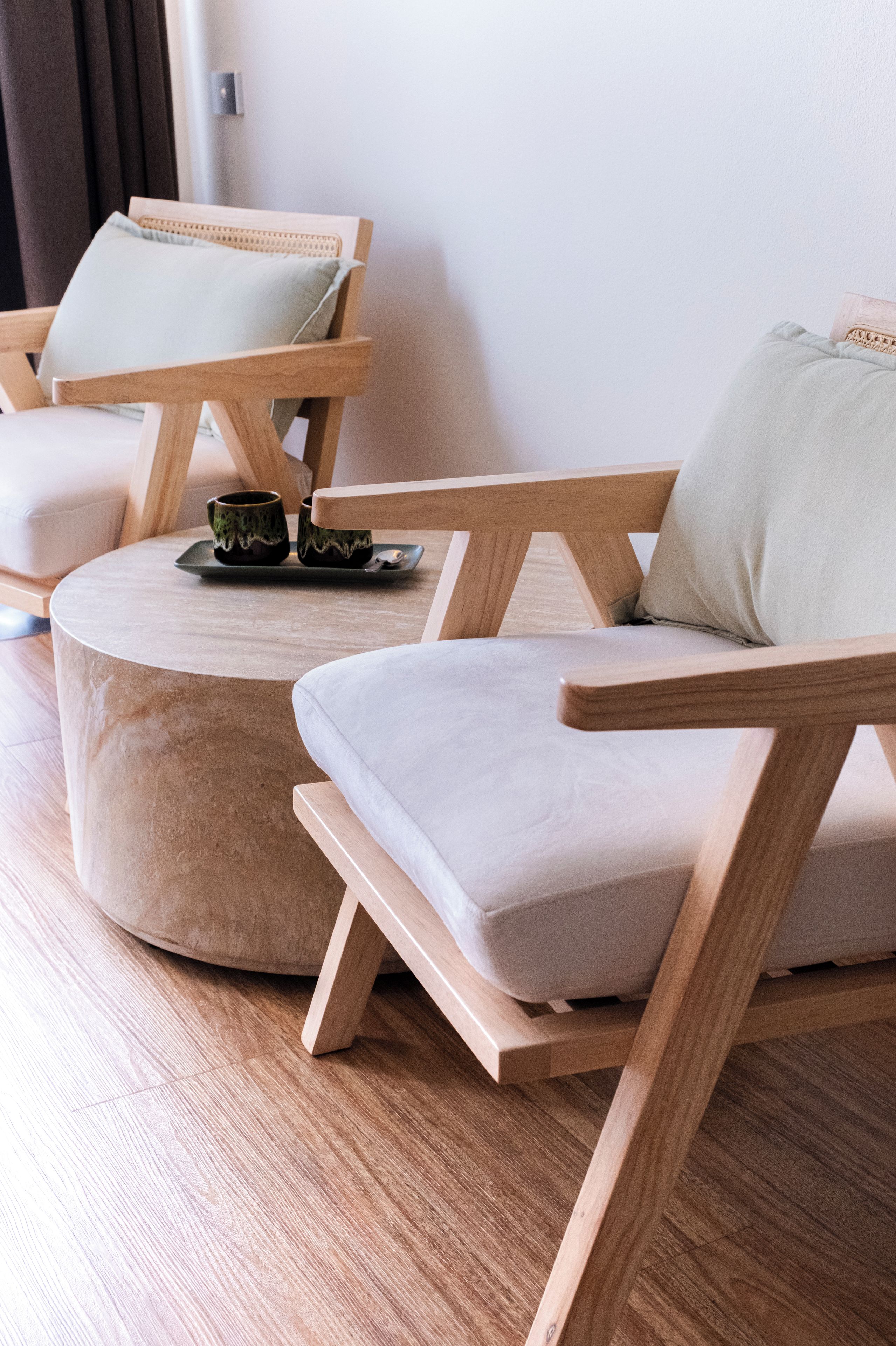 Un salon moderne avec un pouf rond, deux fauteuils en bois et une petite table sur laquelle se trouvent une tasse et une soucoupe.