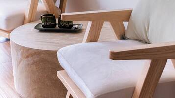 Un salon moderne avec un pouf rond, deux fauteuils en bois et une petite table sur laquelle se trouvent une tasse et une soucoupe.