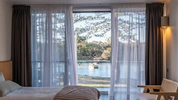 A hotel room with a bed, a chair, and a view of a lake with a boat.