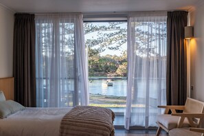 Habitación de hotel con cama, una silla y vista a un lago con un bote.