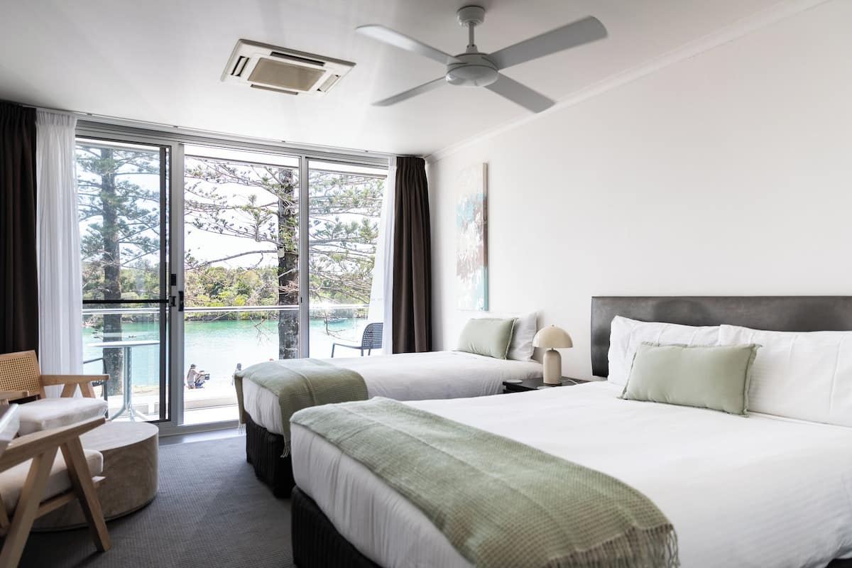 Ein Hotelzimmer mit zwei Betten, einem Balkon mit Meerblick und einem Deckenventilator.