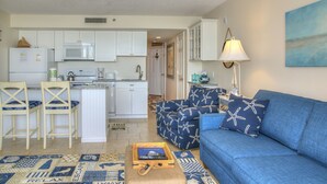A compact living space with a kitchenette, a blue sofa with starfish-patterned cushions, and a small wooden coffee table.