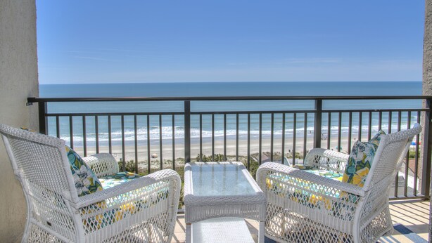 A balcony with wicker furniture overlooking a beach.