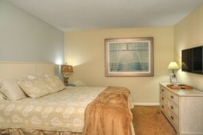 A bedroom with a bed, a nightstand, a dresser, a TV, and a framed picture on the wall.