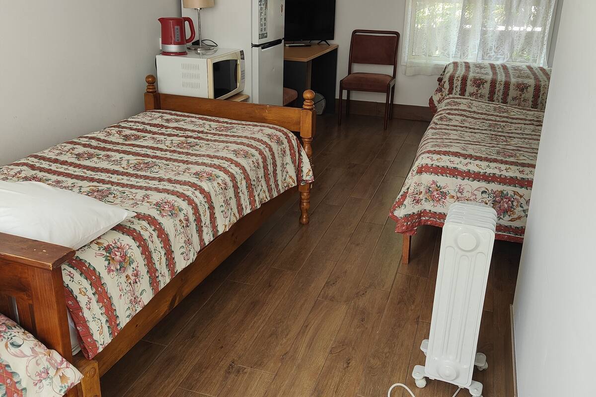Una habitación con dos camas de madera, un escritorio con computadora, una silla y un radiador.