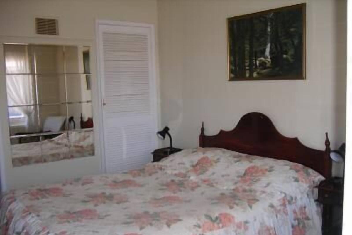 Un dormitorio con una cama de madera, una mesita de noche, un espejo y una puerta.