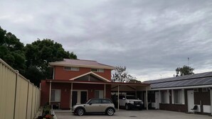 Un bâtiment doté d’un espace de stationnement couvert, une voiture beige et un VUS blanc.
