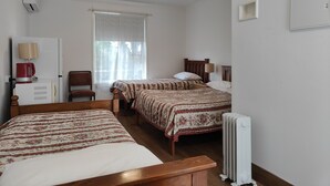Une chambre avec deux lits, un radiateur, un bureau avec une lampe, une chaise et une fenêtre avec des rideaux.