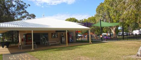A covered outdoor area with a playground, benches, and a vending machine.