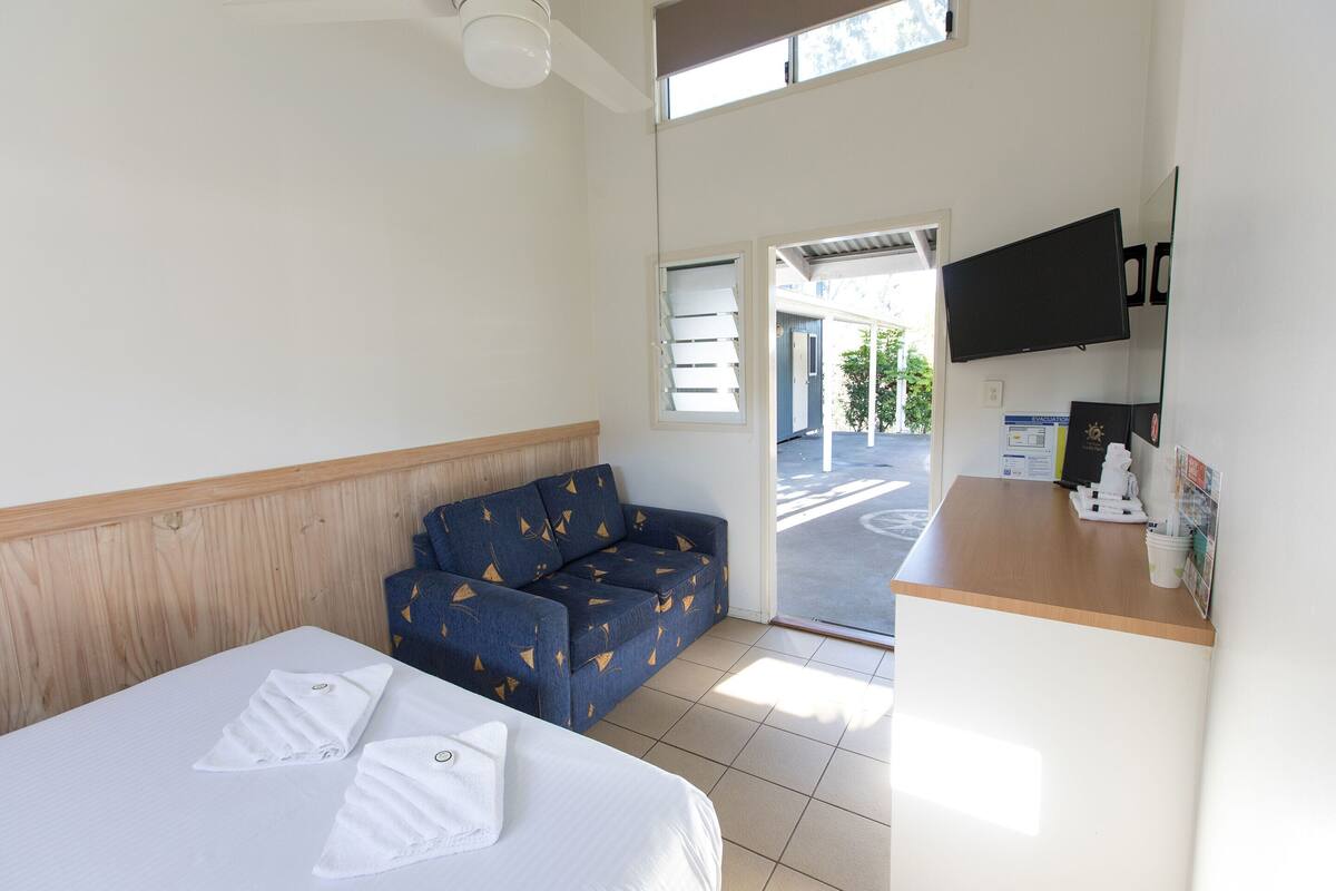 Une chambre d’hôtel avec un lit, un canapé bleu, une tête de lit en bois, un téléviseur à écran plat et un comptoir de réception.