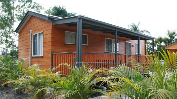 A wooden cabin with a porch, surrounded by tropical plants. - Charters Towers Tourist Park (Mosman Park)