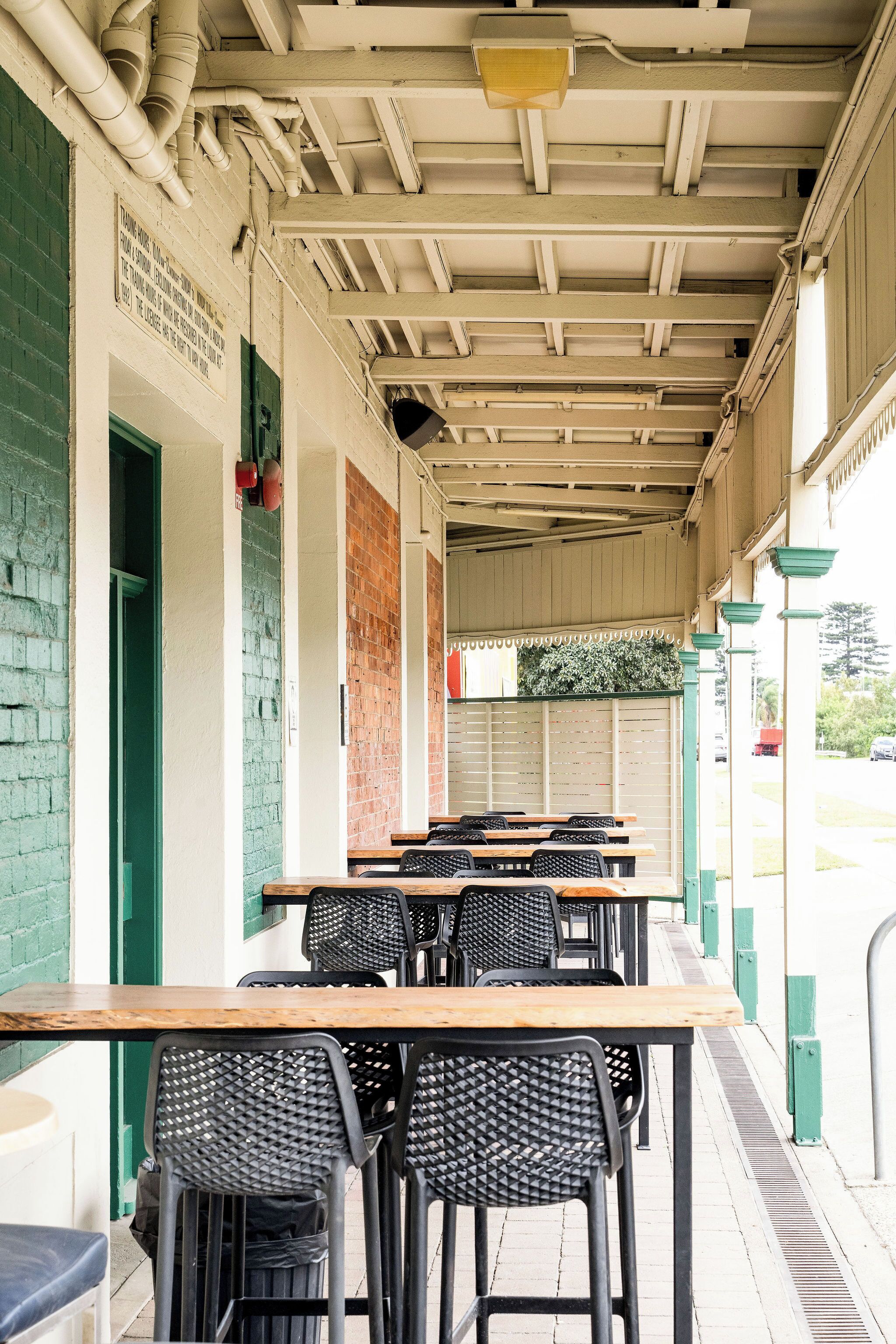 An outdoor seating area with tables and chairs, a covered roof, and a brick wall.