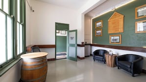 A hotel lobby with a wooden barrel, two leather armchairs, a green door labeled 'PUBLIC BAR', and framed historical photos on the wall.