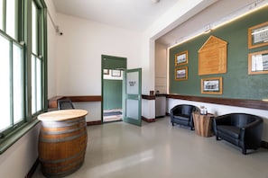 A hotel lobby with a wooden barrel, two leather armchairs, a green door labeled 'PUBLIC BAR', and framed historical photos on the wall.