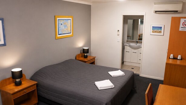 Hotelkamer met een bed, nachtkastjes met lampen, een bureau, een stoel, een badkamer met wastafel en spiegel, en een ingelijste foto aan de muur.