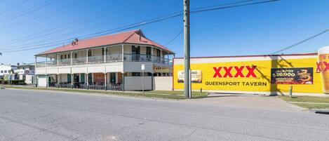 A building with a balcony, a sign for a tavern, and a large yellow advertisement.